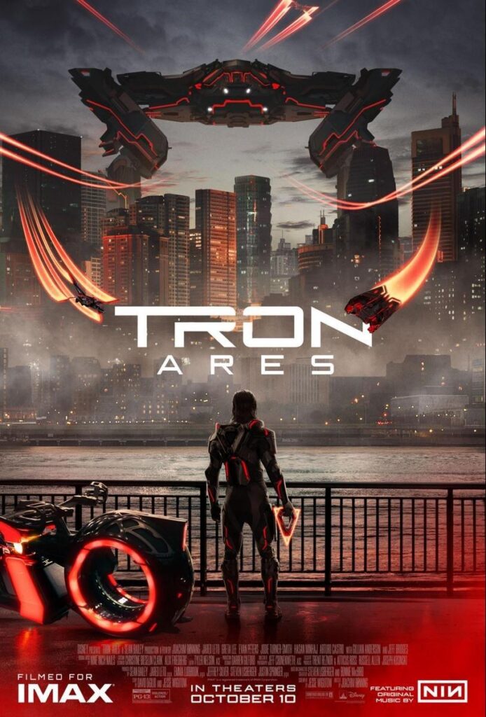 A poster for Tron: Ares. It shows the titular character looking out over a bay in front of a city, over which a Recognizer and a bunch of flying thingies are looming. He holds a triangular Identity Disc, and next to him a Light Cycle is parked. Every single Tron-Element displays red markings, and a red haze colours the picture.