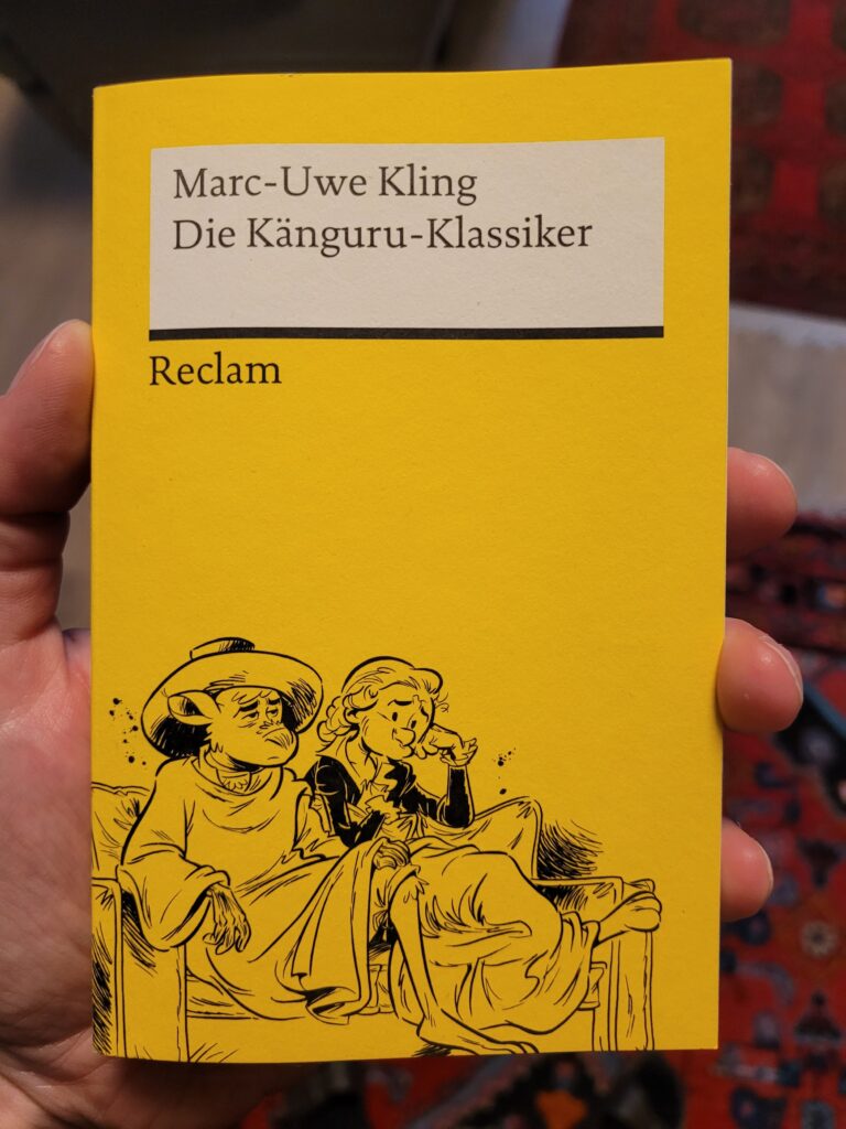 Ein typisches gelbes Reclam-Cover, als Illustration auf einer Couch sitzend das Känguru als Marx in Italien und der Autor als Engels.
