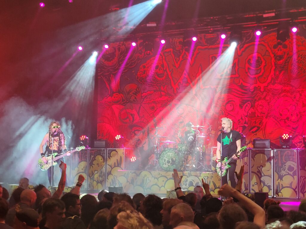 Ein Photo des WiZo-Konzerts: im Vordergrund die Menge, auf der Bühne die Band, dahinter halbwegs erkennbar der Zombie-Backdrop.