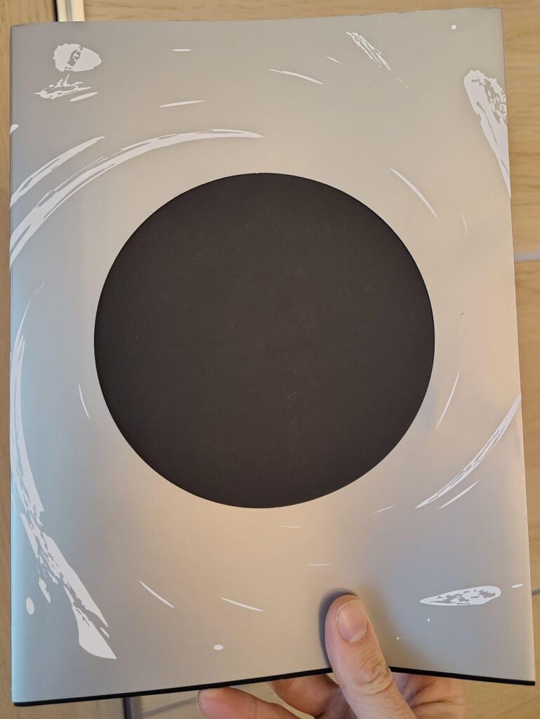 The "cover" of the Outer Wilds Design Works, written by Chris Schilling and published by lostincult.
It shows the silver jacket with a big round cutout in the middle, revealing the black actual cover as if it were a black hole. Around it, several of the in-game symbols for the in-game planets are spagettifying.